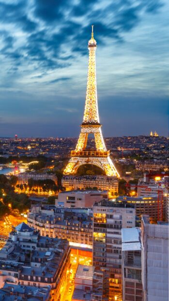 Illuminated Eiffel Tower rising above Paris cityscape at dusk with vibrant street lights and cloudy sky