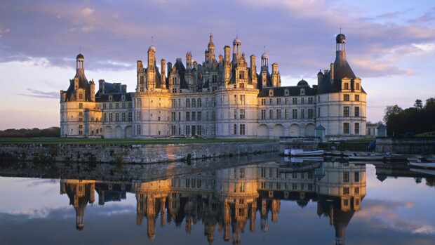 A historic castle in France reflected on calm water during sunset showing France architecture