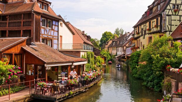 A charming riverside village in France with colorful houses and people dining outdoors along the canal