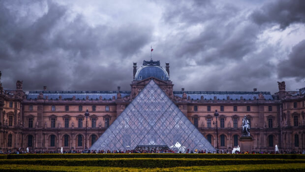 The Louvre Museum with glass pyramid under dramatic clouds in France