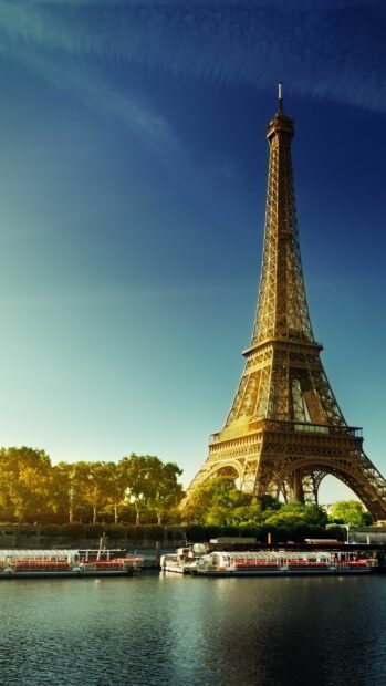The Eiffel Tower in France stands tall by the river surrounded by green trees under a clear blue sky