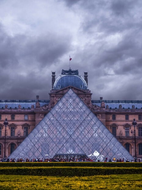The Louvre pyramid surrounded by historic architecture in France on a cloudy day