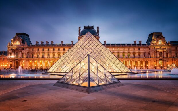 The Louvre pyramid in France illuminated at dusk with historic architecture in the background