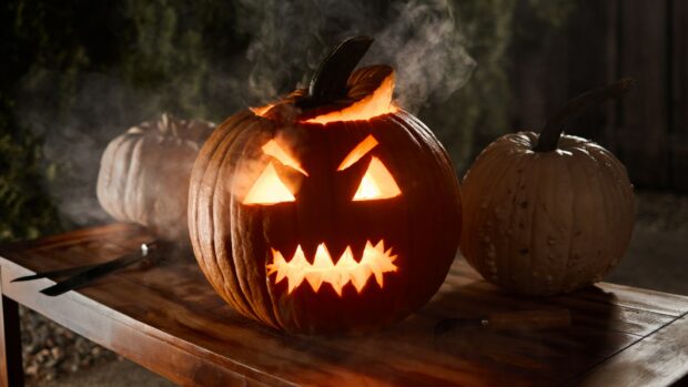 A scary carved jack o' lantern glows and smokes in the dark for Halloween 2025