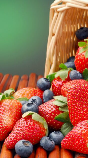 A basket overflows with fresh strawberries and blueberries on a wooden surface, 4K Phone Wallpaper