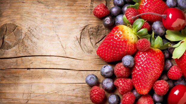 A close up of fresh vibrant berries including strawberries, raspberries, blueberries, and cherries on rustic wood, 2K Desktop Wallpaper