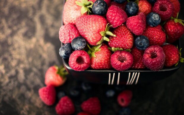 A bowl filled with fresh strawberries, raspberries, and blueberries on a dark surface, HD Desktop Wallpaper