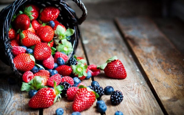 A basket spills fresh strawberries, raspberries, blueberries, and blackberries onto a wooden surface, 2K Desktop Wallpaper