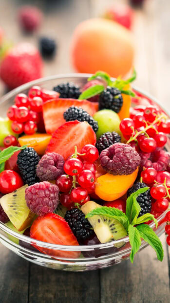 A close up of fresh colorful berries in a glass bowl with mint leaves on a wooden table, HD Mobile Wallpaper