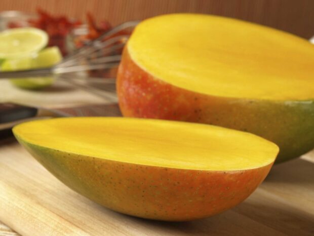 Two fresh ripe mango halves are placed on a wooden surface in a kitchen setting, HD Desktop Wallpaper
