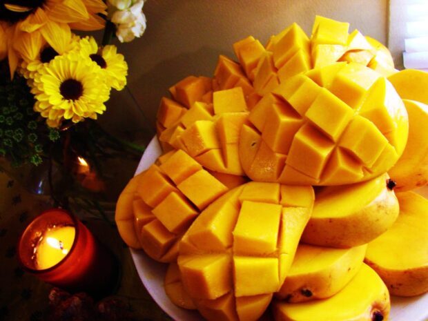Fresh ripe mangoes cut into cubes placed on a plate with flowers and a candle nearby, HD Desktop Wallpaper