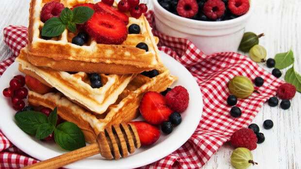 A plate of fresh waffles topped with strawberries, raspberries, blueberries, and honey served with berries on a checkered cloth, HD Desktop Wallpaper