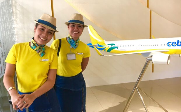 Two Cebu Pacific Air attendants stand near a model airplane smiling warmly, 2K Desktop Wallpaper