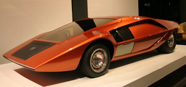A sleek orange Lancia car with a futuristic design displayed indoors, 2K Desktop Wallpaper