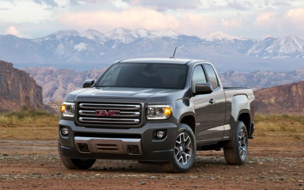 A gray GMC truck is parked on rocky ground with mountains in the background under a cloudy sky, 2K Desktop Wallpaper