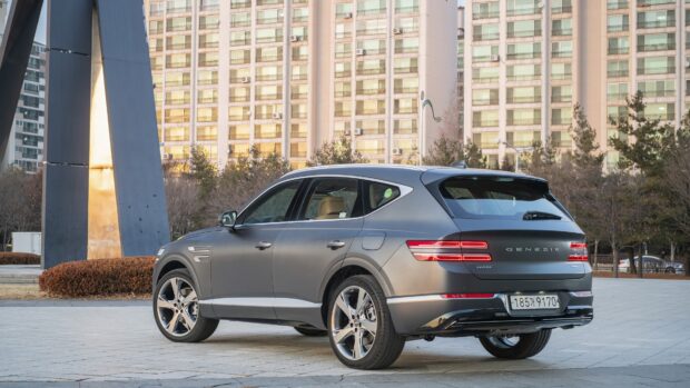 A sleek Genesis car is parked on a paved area next to a modern building during sunset, 4K Desktop Wallpaper