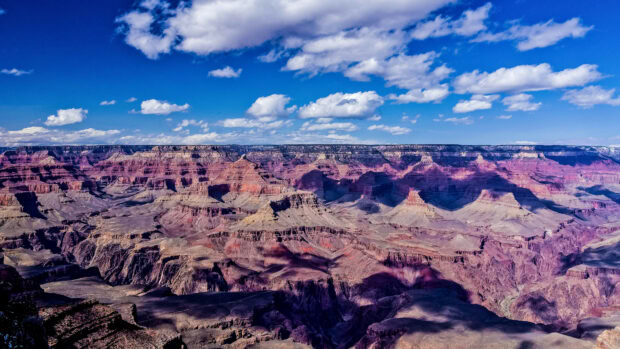 Geological formations of the Grand Canyon under a bright blue sky with scattered clouds