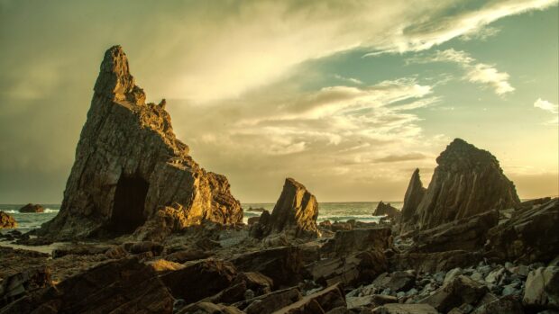 Jagged geology formations on rocky coast under cloudy sky at sunset