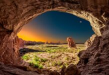 A natural arch frames a vast geology landscape with rock formations and clear sky