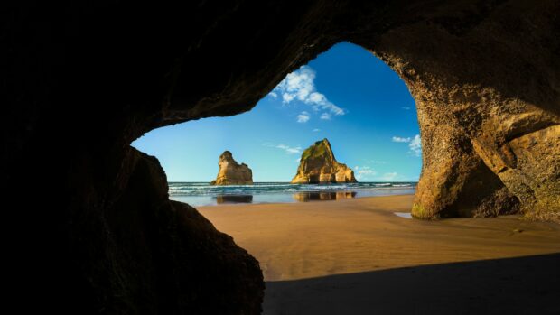 View of geological rock formations on a sandy beach through a cave opening