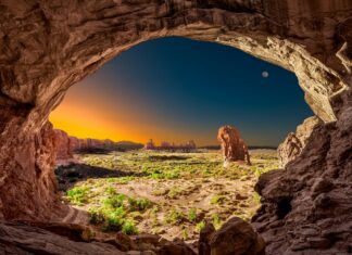 A natural arch frames a vast geology landscape with rock formations and clear sky