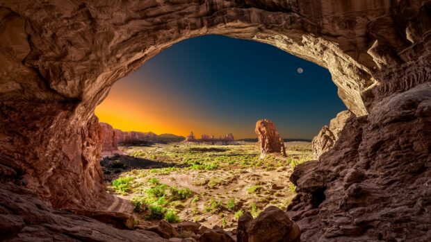 A natural arch frames a vast geology landscape with rock formations and clear sky