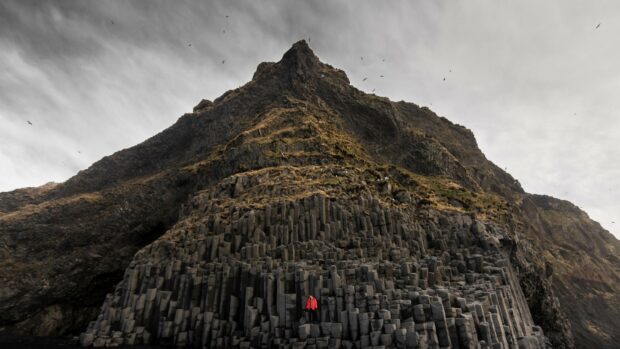 Basalt columns formation showcasing unique geology with a person standing in a red jacket