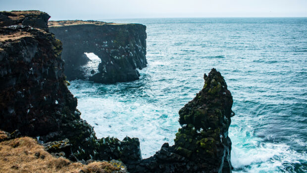 A rugged coastline with volcanic rock formations showing geology next to the ocean waves