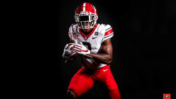 A Georgia Bulldogs player wearing red and white uniform holding a football in action