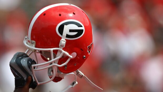 A close up of a Georgia Bulldogs helmet held by a gloved hand