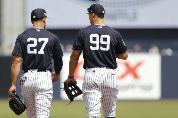 Two baseball players wearing pinstriped pants and dark jerseys walking on the field including Giancarlo Stanton jersey number 99