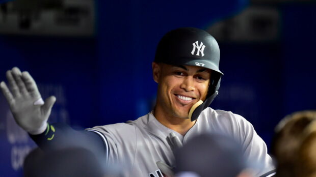 Giancarlo Stanton smiling and high fiving teammates in New York Yankees uniform