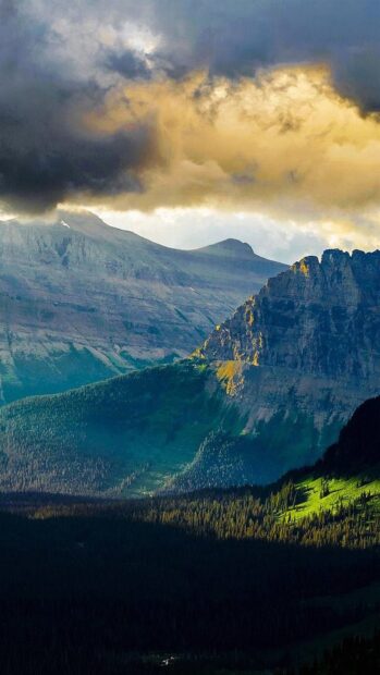 The Glacier National Park mountains are illuminated by golden sunset light under dramatic clouds, 4K Phone Wallpaper