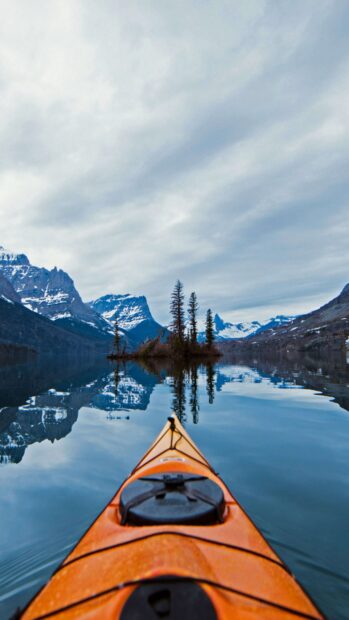 A kayak floats peacefully on a calm lake surrounded by snow capped mountains in Glacier National Park, 4K Phone Wallpaper