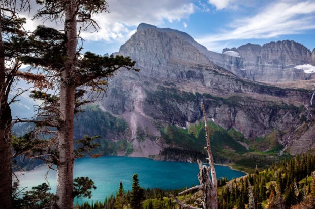 A scenic view of Glacier National Park with a blue lake and rocky mountains under a partly cloudy sky, HD Desktop Wallpaper