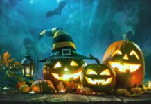 Spooky Halloween pumpkins with glowing faces, autumn leaves, lantern, witch hat, and bat on dark wooden surface with mysterious blue background.