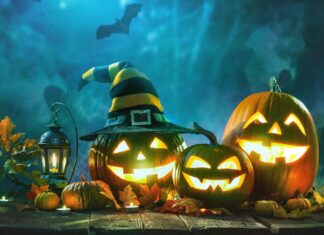 Spooky Halloween pumpkins with glowing faces, autumn leaves, lantern, witch hat, and bat on dark wooden surface with mysterious blue background.