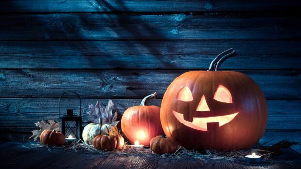A glowing Halloween pumpkin with carved face is surrounded by other pumpkins and candles, 4K Desktop Wallpaper