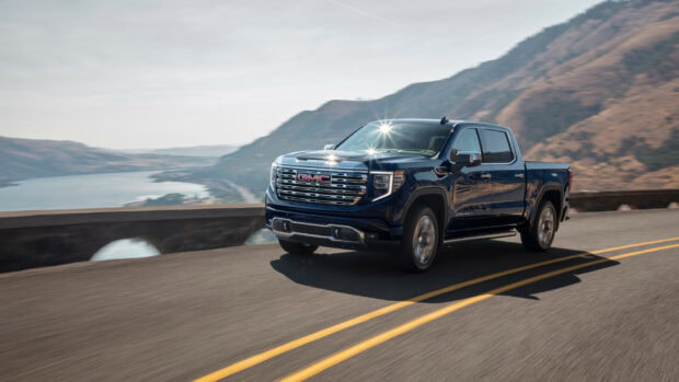 A dark blue GMC truck is driving on a road with mountains and a river in the background, HD Desktop Wallpaper