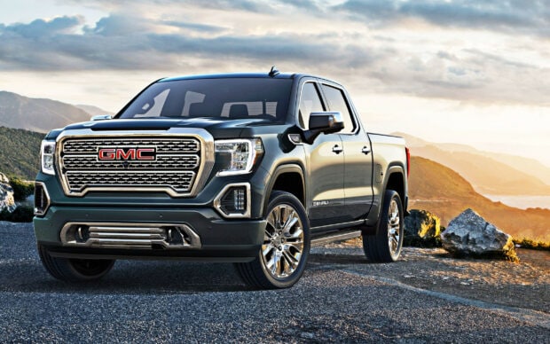 A GMC pickup truck is parked on a mountain road during sunset featuring rugged terrain and scenic views, 2K Desktop Wallpaper