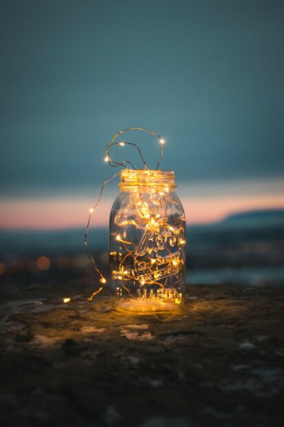 Glass jar filled with gold lights on a rocky surface at dusk