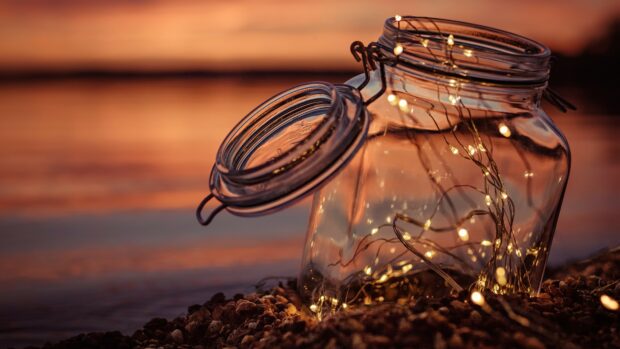 Glass jar filled with gold lights on rocky surface at sunset with gold lights glow