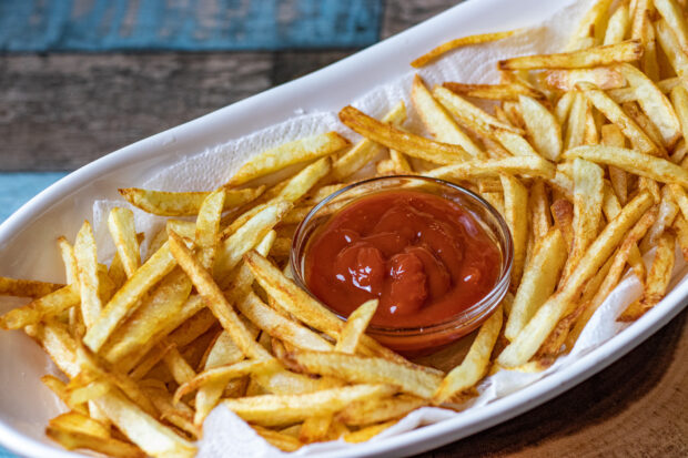 A plate of golden French fries surrounds a bowl of ketchup on a wooden table, HD Desktop Wallpaper