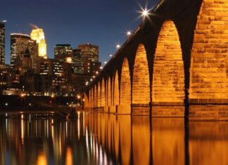 The Mississippi River shows glowing arches on the bridge reflecting in calm water at night