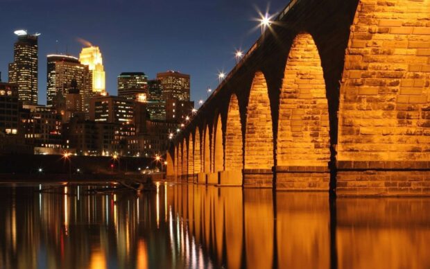 The Mississippi River shows glowing arches on the bridge reflecting in calm water at night