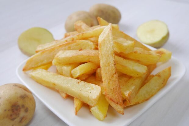 A close up view of golden crispy french fries served on a white plate with raw potatoes in the background, HD Desktop Wallpaper