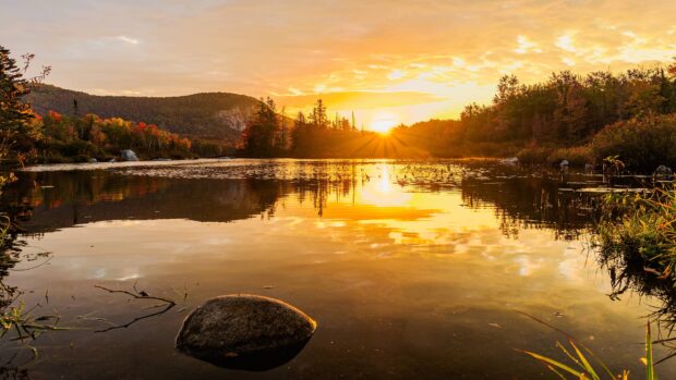 A golden sunset shines over a calm lake surrounded by Vermont trees and hills, 4K Desktop Wallpaper
