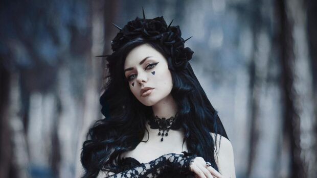A goth woman with black floral headpiece and heart makeup on her cheeks in a forest setting