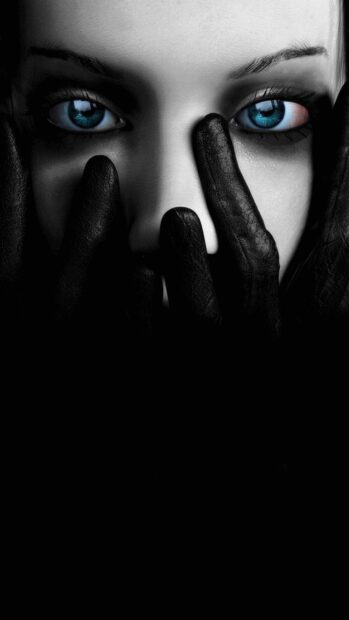 A goth face with blue eyes partially covered by black leather gloves creating a mysterious look