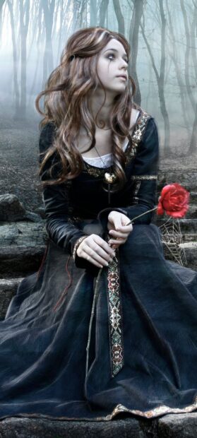 Goth style woman holding a red rose sitting in a dark forest with long hair and detailed dress